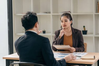 İki Asyalı işadamı başarılı takım çalışmalarının sonuçlarını gösteren çizelge ve grafikleri tartışıyor. İşyerinde çizelge tabletleri ve tabletler kullanılıyor