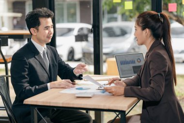 İki Asyalı işadamı başarılı takım çalışmalarının sonuçlarını gösteren çizelge ve grafikleri tartışıyor. İşyerinde çizelge tabletleri ve tabletler kullanılıyor