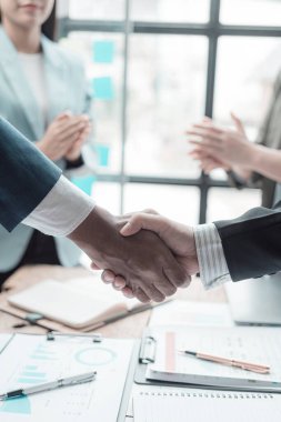 İş ekibi ofisinde ve sözleşme imzaladıktan sonra el sıkışıyorlar. İş arkadaşları ofiste dizüstü bilgisayar ve veri tablosuyla el ele tutuşuyorlar.