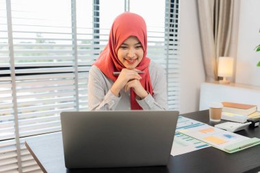 Ofiste dizüstü bilgisayarla çalışan tesettürlü Müslüman bir kadın, masadaki belgeler, planlama, analiz, mali rapor, iş planı, yatırım.