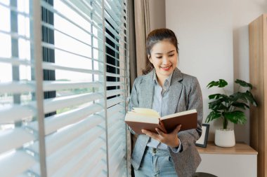 Asyalı iş kadını finansal tabloları analiz ediyor ve dizüstü bilgisayarını pano ve kalemle kullanıyor. Ofiste yalnız çalışıyor.