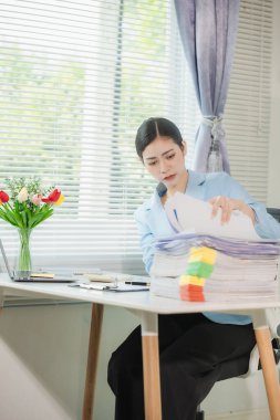 Masasında belgeler ve dosyalarla çalışan bir kadın var. Belgeleri düzenlemek, mali bilgileri gözden geçirmek. Masasında bir yığın belge tutarken önemli belgeleri inceliyor..