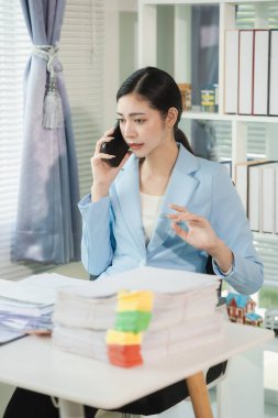 Asyalı işadamı dizüstü bilgisayarda çalışıyor ve telefonda konuşurken çizelgeler ve grafiklerle birlikte oturuyor. Verimli çalışma günü, dikey resimleme