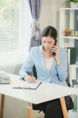 Asyalı işadamı dizüstü bilgisayarda çalışıyor ve telefonda konuşurken çizelgeler ve grafiklerle birlikte oturuyor. Verimli çalışma günü, dikey resimleme