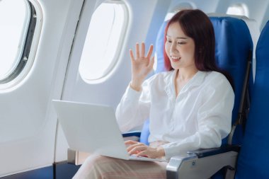 Genç bir kadın iş gezisi sırasında uçakta rahat bir şekilde seyahat ederken dizüstü bilgisayar kullanıyor. İş ve ulaşım kavramı.