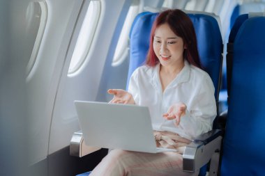 Genç bir kadın iş gezisi sırasında uçakta rahat bir şekilde seyahat ederken dizüstü bilgisayar kullanıyor. İş ve ulaşım kavramı.