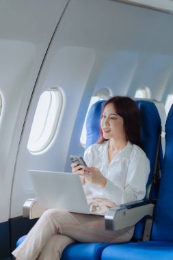 Genç bir kadın iş gezisi sırasında uçakta rahat bir şekilde seyahat ederken dizüstü bilgisayar kullanıyor. İş ve ulaşım kavramı.