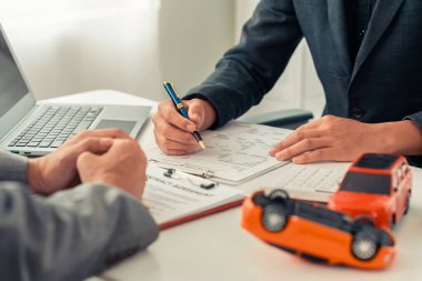 Sigorta acentesinin eli masadaki kırmızı oyuncak arabayı koruyor. Ulaşım finansmanını yönetmeyi planlıyorum. Araba sigortası konsepti.