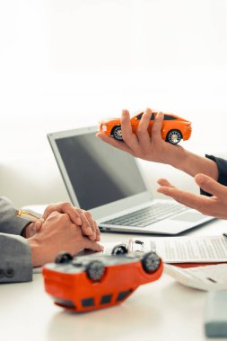 Sigorta acentesinin eli masadaki kırmızı oyuncak arabayı koruyor. Ulaşım finansmanını yönetmeyi planlıyorum. Araba sigortası konsepti.