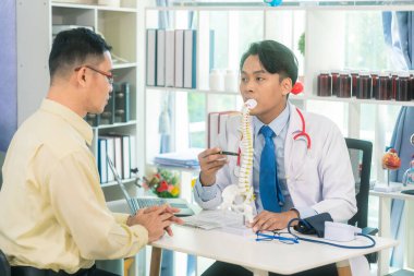 Steteskoplu beyaz üniformalı erkek doktor hastaya, iskelet modeline, sağlık hizmetine ve sağlıklı yaşam konseptine sırt sorununu açıklıyor.