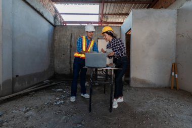 Asyalı endüstriyel erkek ve kadın mühendisler toplanıyor, makine planlarını analiz ediyor, inşaat alanındaki ofis masasında projeleri tartışıyorlar..