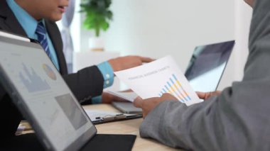 Grafik belgesindeki verileri analiz eden ve ortaklarla toplantıda görüşleri paylaşan bir iş adamı. Yönetici eğilimleri tanımlıyor, iş sorunları.