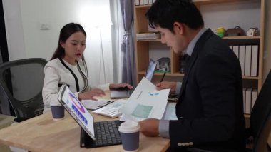 Asyalı iş çifti gece finans toplantısı yapıyor. Oturma odasında ev finansmanı planlıyorlar. Konferans masasında çalışırken dizüstü bilgisayar ve tablet kullanıyorlar.