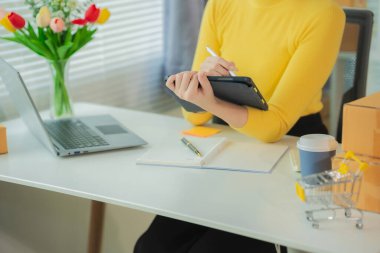 KOBİ tedarik zinciri kavramı, satın alma, Asyalı kadın girişimci dizüstü bilgisayar üzerinde çalışırken not alıyor, müşteri küçük işletme mağazalarında siparişleri yönetiyor.