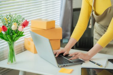 KOBİ tedarik zinciri kavramı, satın alma, Asyalı kadın girişimci dizüstü bilgisayar üzerinde çalışırken not alıyor, müşteri küçük işletme mağazalarında siparişleri yönetiyor.