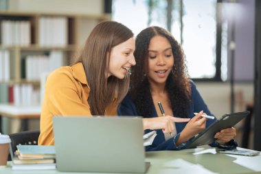 İki iş kadını dizüstü bilgisayarlarda birlikte çalışıyor, bilgisayarlara bakıyor, internette yapay zeka projelerini tartışıyor, ofislerdeki masalarda oturuyor..