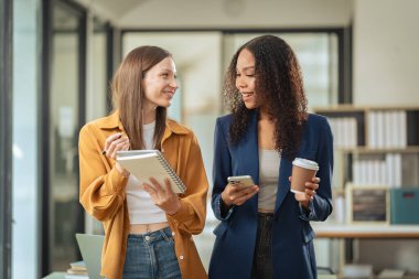 İki iş kadını dizüstü bilgisayarlarda birlikte çalışıyor, bilgisayarlara bakıyor, internette yapay zeka projelerini tartışıyor, ofislerdeki masalarda oturuyor..