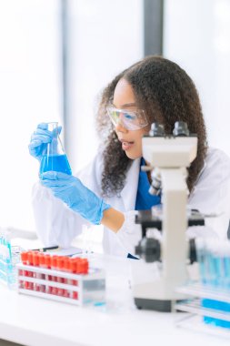 Afrikalı Amerikalı bir kadın bilim adamı mikroskop ile klinik laboratuvar deneyleri yapıyor ve kök hücre araştırmaları üzerinde laboratuvar analizleri yapıyor..