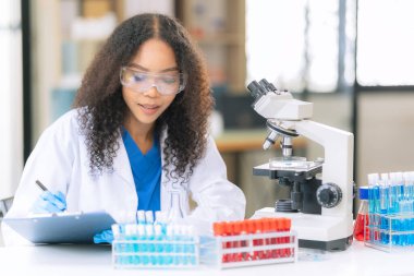 Afrikalı Amerikalı bir kadın bilim adamı mikroskop ile klinik laboratuvar deneyleri yapıyor ve kök hücre araştırmaları üzerinde laboratuvar analizleri yapıyor..