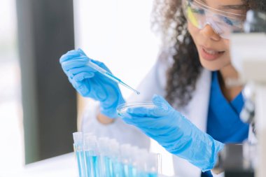 Afrikalı Amerikalı bir kadın bilim adamı mikroskop ile klinik laboratuvar deneyleri yapıyor ve kök hücre araştırmaları üzerinde laboratuvar analizleri yapıyor..