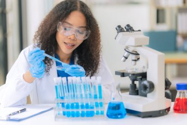 Afrikalı Amerikalı bir kadın bilim adamı mikroskop ile klinik laboratuvar deneyleri yapıyor ve kök hücre araştırmaları üzerinde laboratuvar analizleri yapıyor..