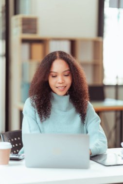 Dijital tablet ve dizüstü bilgisayar kullanan genç Afrikalı Amerikalı kadın ofiste çalışıyor.