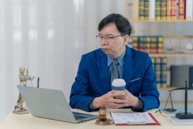 Masasında dizüstü bilgisayarla çalışan bir avukat ya da muhasebeci keskin bir takım elbise içindeki dava dosyalarını inceliyor ve masasında oturuyor..