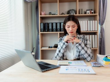Ofisteki dizüstü bilgisayarda çalışırken elinde kalem tutan ve mali belgeleri analiz eden Asyalı iş kadını..