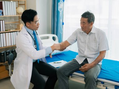 Yetenekli bir erkek fizyoterapist yaşlı bir erkek hastayı muayene ediyor. Yatakta yatıyor. Hastane muayene odasında kas gücünü kontrol ediyor..