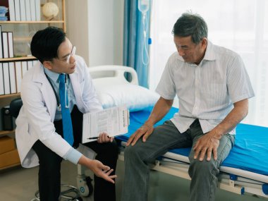 Yetenekli bir erkek fizyoterapist yaşlı bir erkek hastayı muayene ediyor. Yatakta yatıyor. Hastane muayene odasında kas gücünü kontrol ediyor..