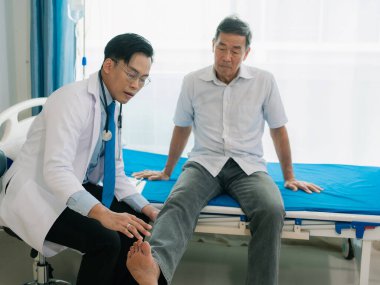 Yetenekli bir erkek fizyoterapist yaşlı bir erkek hastayı muayene ediyor. Yatakta yatıyor. Hastane muayene odasında kas gücünü kontrol ediyor..