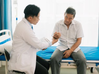 Yetenekli bir erkek fizyoterapist yaşlı bir erkek hastayı muayene ediyor. Yatakta yatıyor. Hastane muayene odasında kas gücünü kontrol ediyor..