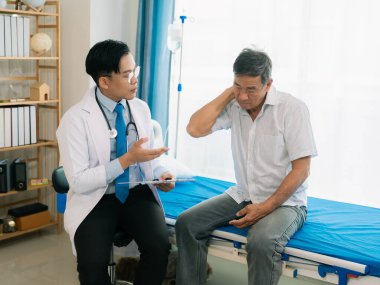Yetenekli bir erkek fizyoterapist yaşlı bir erkek hastayı muayene ediyor. Yatakta yatıyor. Hastane muayene odasında kas gücünü kontrol ediyor..