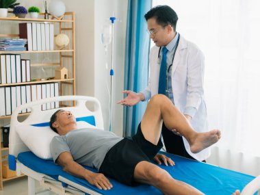 Yetenekli bir erkek fizyoterapist yaşlı bir erkek hastayı muayene ediyor. Yatakta yatıyor. Hastane muayene odasında kas gücünü kontrol ediyor..