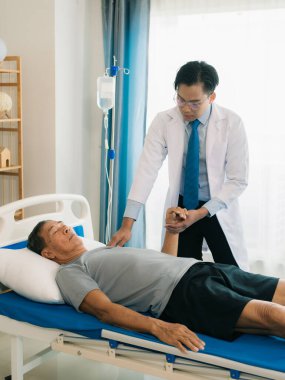 Yetenekli bir erkek fizyoterapist yaşlı bir erkek hastayı muayene ediyor. Yatakta yatıyor. Hastane muayene odasında kas gücünü kontrol ediyor..