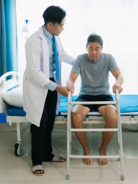 Yetenekli bir erkek fizyoterapist yaşlı bir erkek hastayı muayene ediyor. Yatakta yatıyor. Hastane muayene odasında kas gücünü kontrol ediyor..