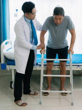 Yetenekli bir erkek fizyoterapist yaşlı bir erkek hastayı muayene ediyor. Yatakta yatıyor. Hastane muayene odasında kas gücünü kontrol ediyor..