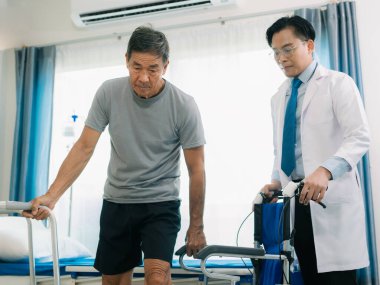 Yetenekli bir erkek fizyoterapist yaşlı bir erkek hastayı muayene ediyor. Yatakta yatıyor. Hastane muayene odasında kas gücünü kontrol ediyor..