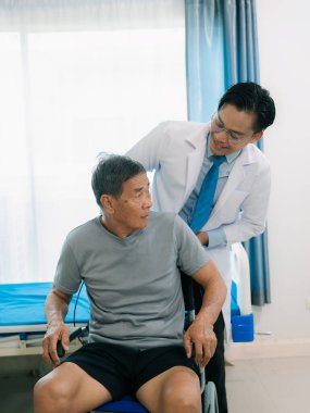 Yetenekli bir erkek fizyoterapist yaşlı bir erkek hastayı muayene ediyor. Yatakta yatıyor. Hastane muayene odasında kas gücünü kontrol ediyor..