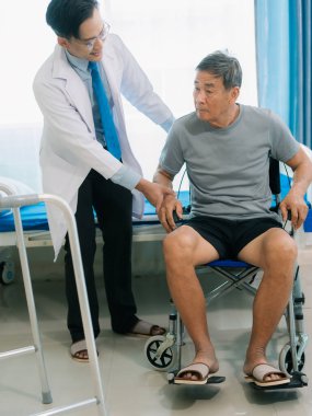 Yetenekli bir erkek fizyoterapist yaşlı bir erkek hastayı muayene ediyor. Yatakta yatıyor. Hastane muayene odasında kas gücünü kontrol ediyor..