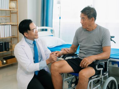 Yetenekli bir erkek fizyoterapist yaşlı bir erkek hastayı muayene ediyor. Yatakta yatıyor. Hastane muayene odasında kas gücünü kontrol ediyor..