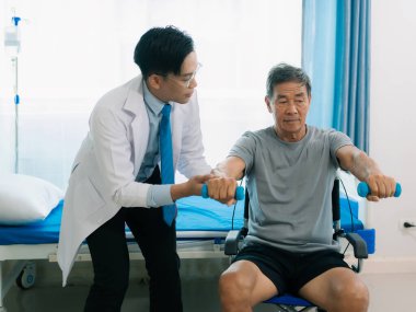 Asyalı fizyoterapist ve tekerlekli sandalyedeki yaşlı hasta halter kemeri tutuyor. Dambılı sağlık hizmeti. Yaşlı insanlar yaşlanıyor. Uyumlu spor aktiviteleri.