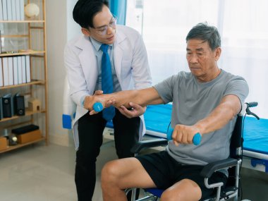 Asyalı fizyoterapist ve tekerlekli sandalyedeki yaşlı hasta halter kemeri tutuyor. Dambılı sağlık hizmeti. Yaşlı insanlar yaşlanıyor. Uyumlu spor aktiviteleri.