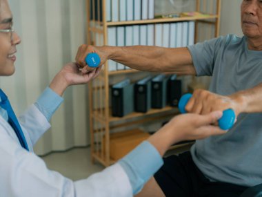 Asyalı fizyoterapist ve tekerlekli sandalyedeki yaşlı hasta halter kemeri tutuyor. Dambılı sağlık hizmeti. Yaşlı insanlar yaşlanıyor. Uyumlu spor aktiviteleri.