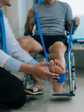 Kıdemli Asyalı adam ayak kaslarını esnetmek için direnç bandı kullanıyor. Evde bakıcı ile egzersiz yapma fizyoterapi konsepti.