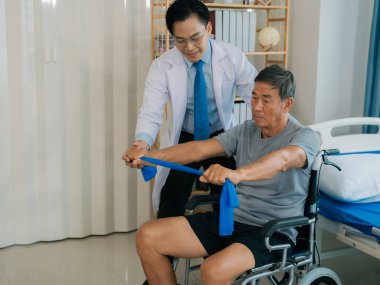 Yetenekli bir erkek fizyoterapist yaşlı bir erkek hastayı muayene ediyor. Yatakta yatıyor. Hastane muayene odasında kas gücünü kontrol ediyor..