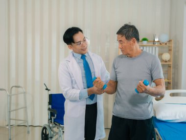 Asyalı fizyoterapist ve tekerlekli sandalyedeki yaşlı hasta halter kemeri tutuyor. Dambılı sağlık hizmeti. Yaşlı insanlar yaşlanıyor. Uyumlu spor aktiviteleri.