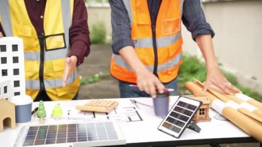 Yelekli ve miğferli iki Asyalı erkek ve kadın mühendis tablet üzerinde birlikte çalışıyor ve mimari yapı tasarımının planlarını tutuyorlar..