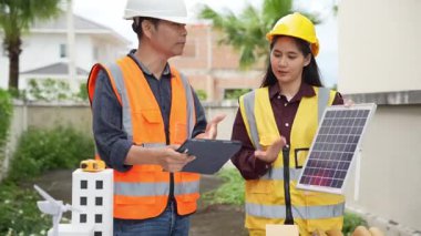 Yelekli ve miğferli iki Asyalı erkek ve kadın mühendis tablet üzerinde birlikte çalışıyor ve mimari yapı tasarımının planlarını tutuyorlar..