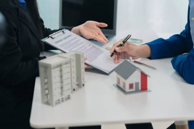 Emlak acentesinin yakın planında müşterilere sigorta sözleşmesi formlarının imzalanması ve ipotek kredisi önerileri sunuluyor..
